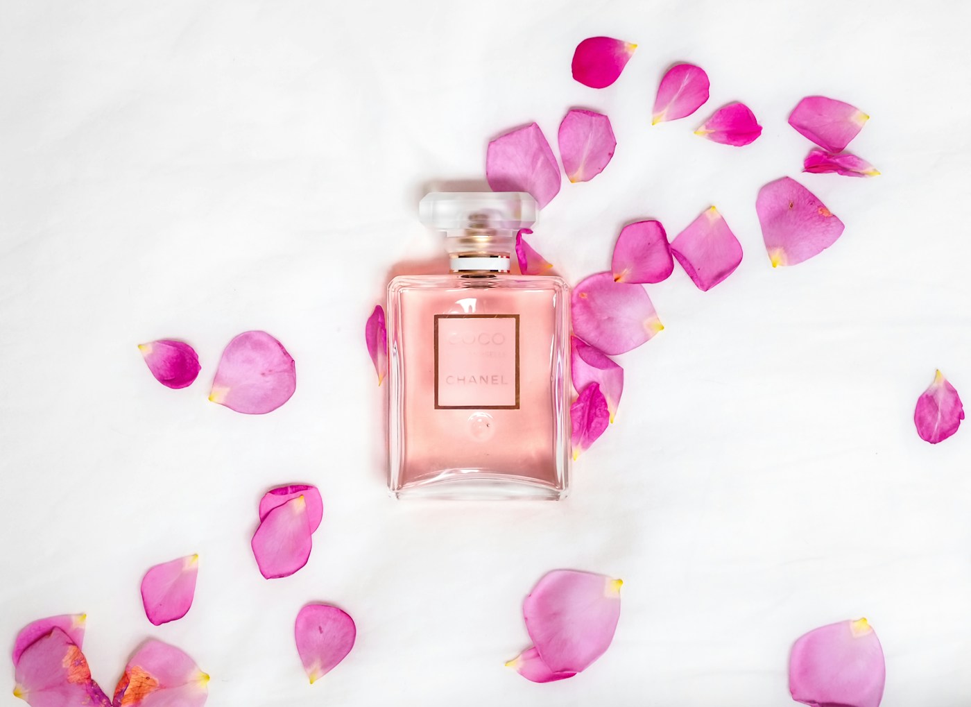 Frasco rosado de perfume Chanel Coco rodeado de pétalos